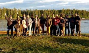Group of guests standing on the riverbank in front of Lake Creek Lodge in Alaska