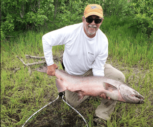 Guest holding a large king salmon on the riverbank near Lake Creek Lodge in Alaska
