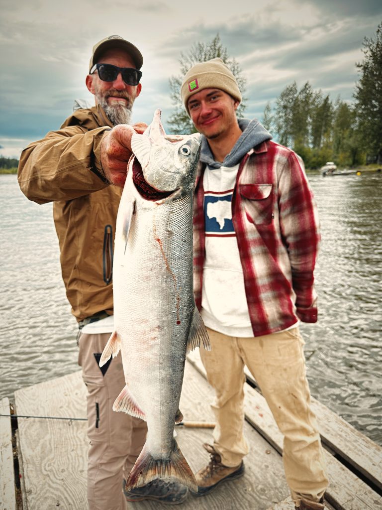 Guests holding a silver salmon off the dock at Lake Creek Lodge in Alaska